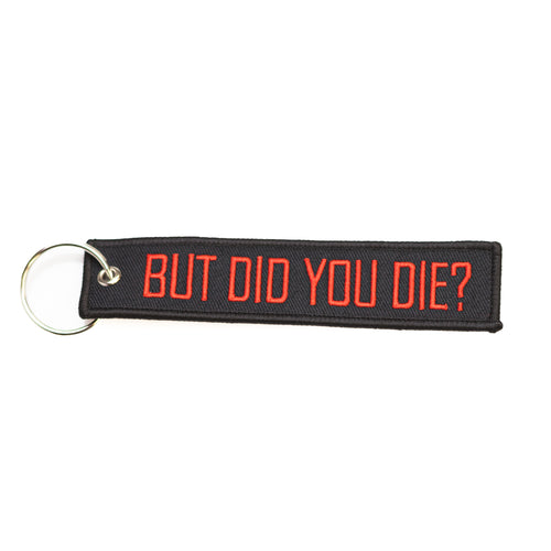A black fabric keychain tag with the phrase 'BUT DID YOU DIE?' embroidered in red. It includes a metal ring for attaching keys.