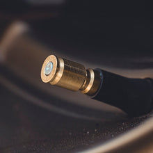 Close-up of a black tire valve stem with a brass-colored metal cap on a dark car wheel.