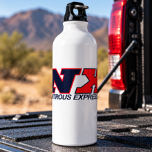 A white aluminum water bottle with a black cap stands on the tailgate of a truck in a desert setting with mountains in the background. The bottle features a red and blue 'NX' logo and the words 'DYNAMIC EXPRESS'.