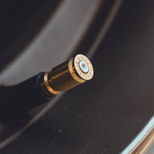 A close-up shot of a metallic bullet casing used as a tire valve tip, resting on a dark textured surface.
