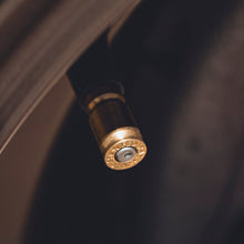 A close-up shot of a metallic gold valve stem on a car tire, set against a dark, blurred background.