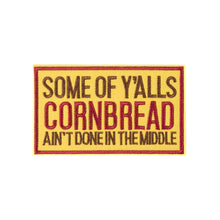 A rectangular embroidered fabric patch with the text 'Some of Y'alls Cornbread Ain't Done In The Middle' on a beige background with a red border.