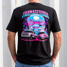 Person wearing a black t-shirt with a colorful graphic design and 'Farmageddon' text, standing against a white corrugated metal wall.