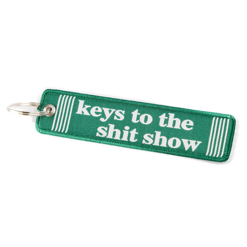 A green embroidered fabric keychain tag with the phrase 'keys to the shit show' in white text.