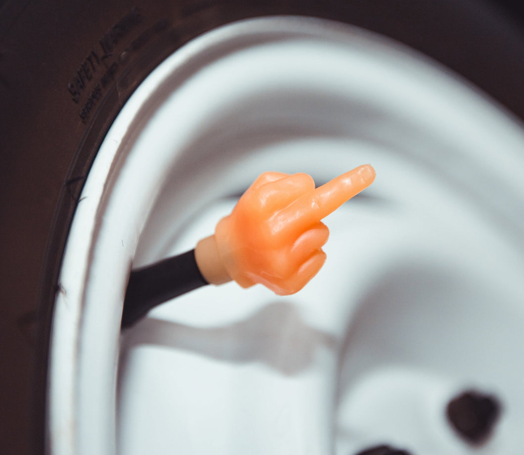 A plastic valve stem cap shaped like a middle finger gesture, orange in color, designed to fit on top of a vehicle's tire valve stem.