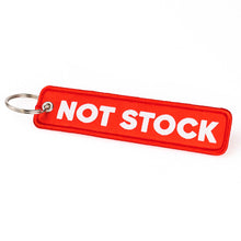 A red rectangular embroidered keychain tag with the words 'NOT STOCK' in bold white capital letters, attached to a silver metal split ring, on a plain white background.