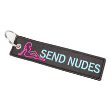 This image features a cheeky and playful keychain designed with the phrase "SEND NUDES" prominently displayed in blue embroidery on a durable black nylon surface. The keychain also includes a pink silhouette of a figure, adding a visual element to the design.