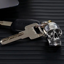 A silver skull-shaped keychain attached to metal keys with a black key fob, resting on a dark ribbed surface.