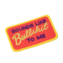 A rectangular embroidered fabric patch with the phrase 'SOUNDS LIKE BULLSHIT TO ME' written in a stylized font, with red background and yellow border.