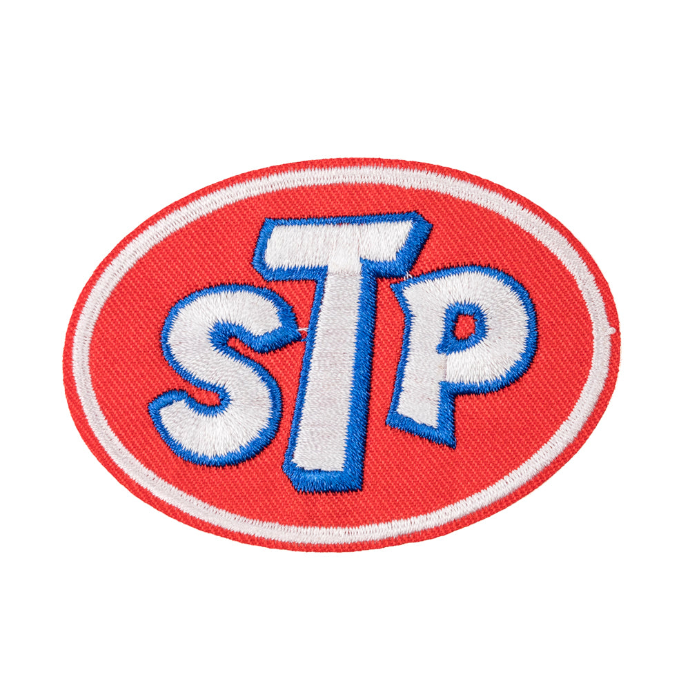 A red, white, and blue embroidered fabric patch with the letters 'STP' in bold blue font centered on a red oval background.