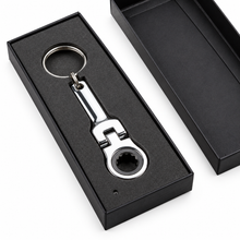 A chrome wrench-shaped keychain with a star drive socket, presented in a black gift box with its lid placed beside it on a white background.